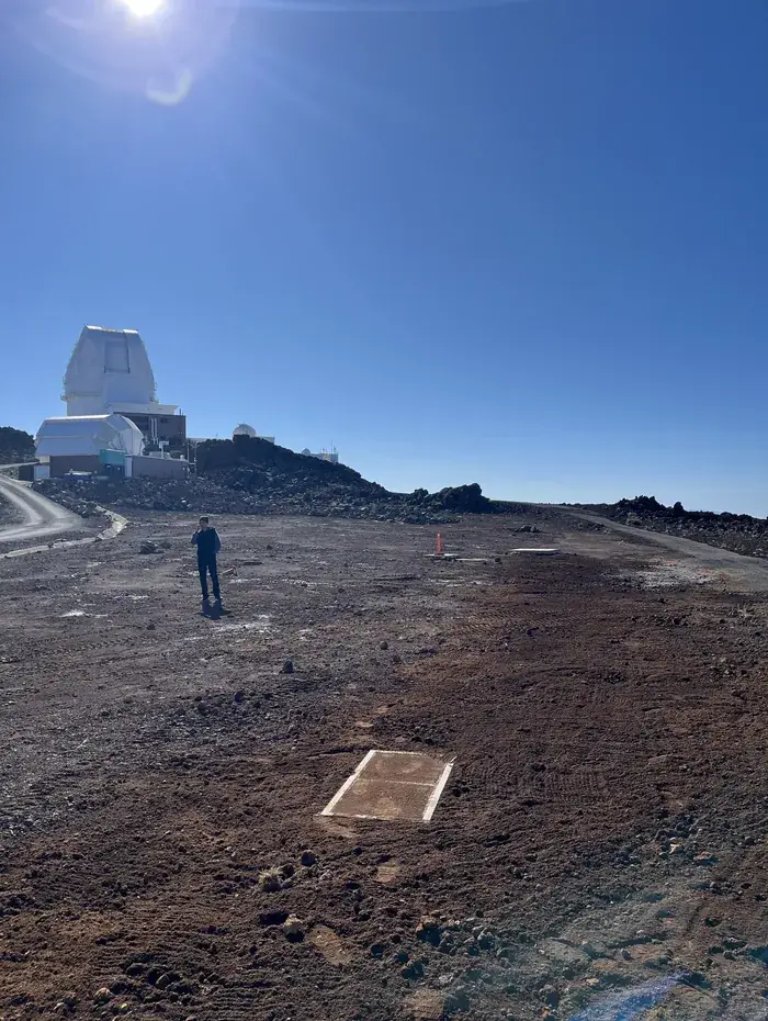 Backfilled and compacted trench line across the volcanic summit of Haleakala, with an observatory dome on the horizon