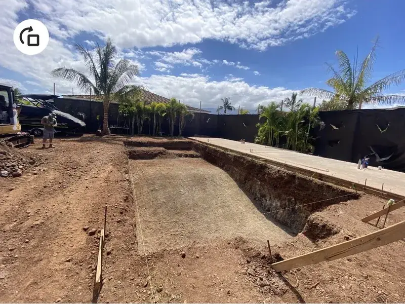 Completed rectangular pool excavation with formed edges, walled yard and palms behind