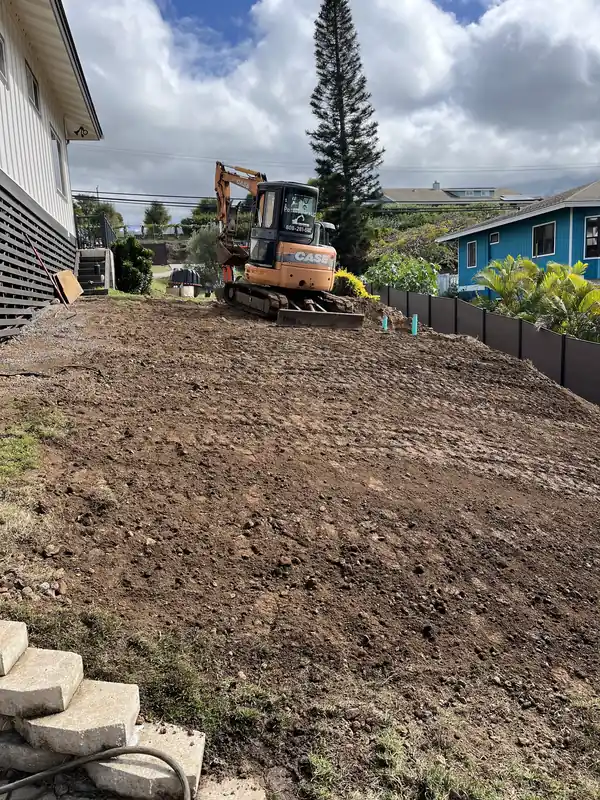 The same yard backfilled and graded smooth after the septic install, excavator parked at the far end