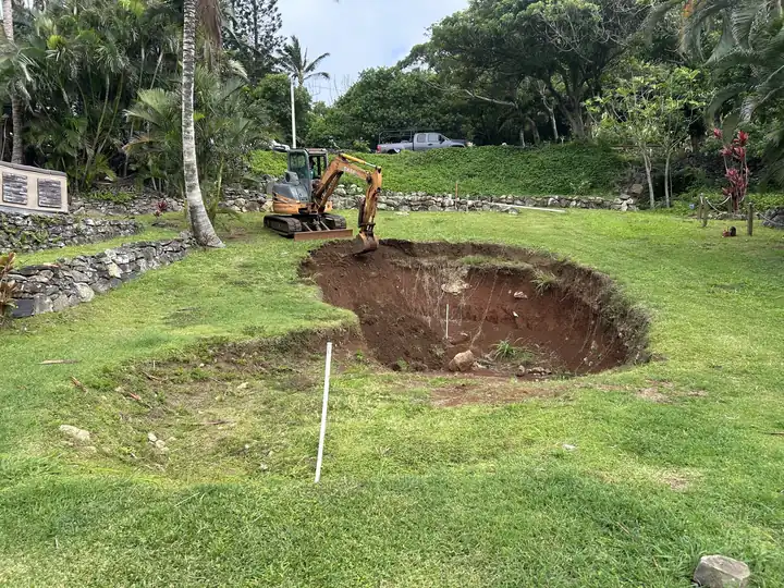 Excavated and shaped hole in a sloped lawn, ready for a waterfall feature, with a mini excavator above